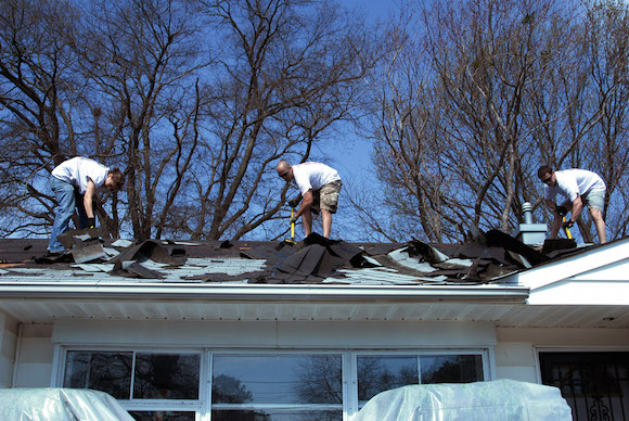 Men on residential roof remove asphalt shingles.