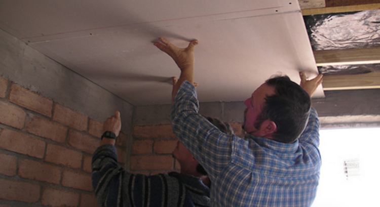 Workers install drywall in ceiling