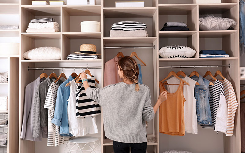 A woman with her back to the camera, arranging clothes in a large, well-organized closet.