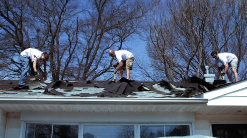 Men on residential roof remove asphalt shingles.